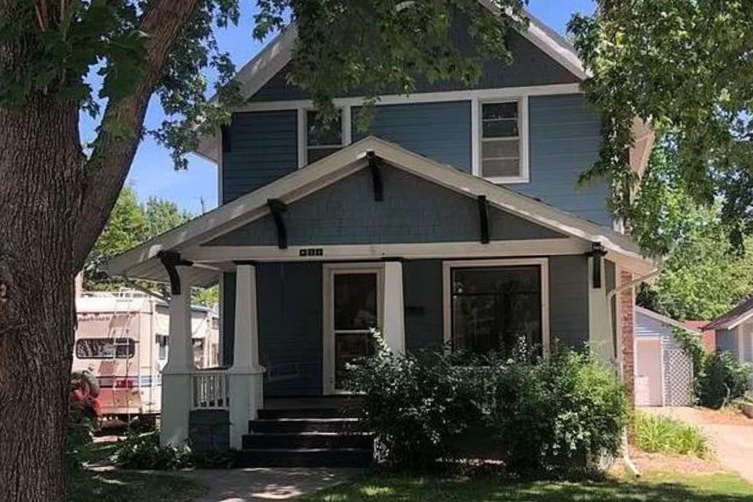 A quaint Cape Cod-style home with beige siding and white window frames, nestled among mature trees in a lush green lawn, located at 2201 S Euclid Ave, Sioux Falls, SD.